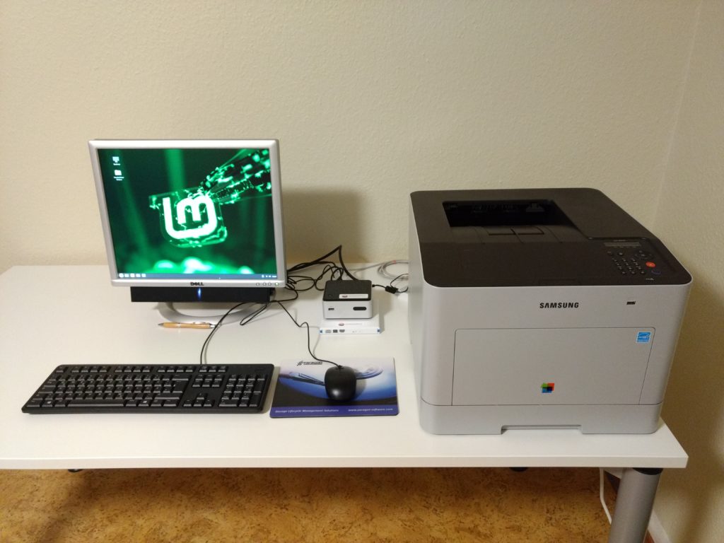 Tisch, auf dem sich ein Komplett-PC mit Eingaberäten und ein Laserdrucker befindet.