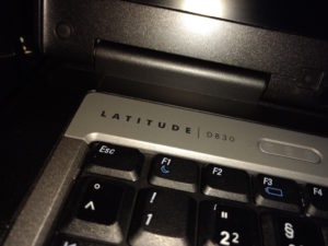 Nahaufnahme der linken, oberen Ecke der Tastatur eines Dell Latitude D830-Laptops, so dass einige Tasten, der Schriftzug der Typbezeichnung und der untere Teil des Bildschirms zu sehen sind.