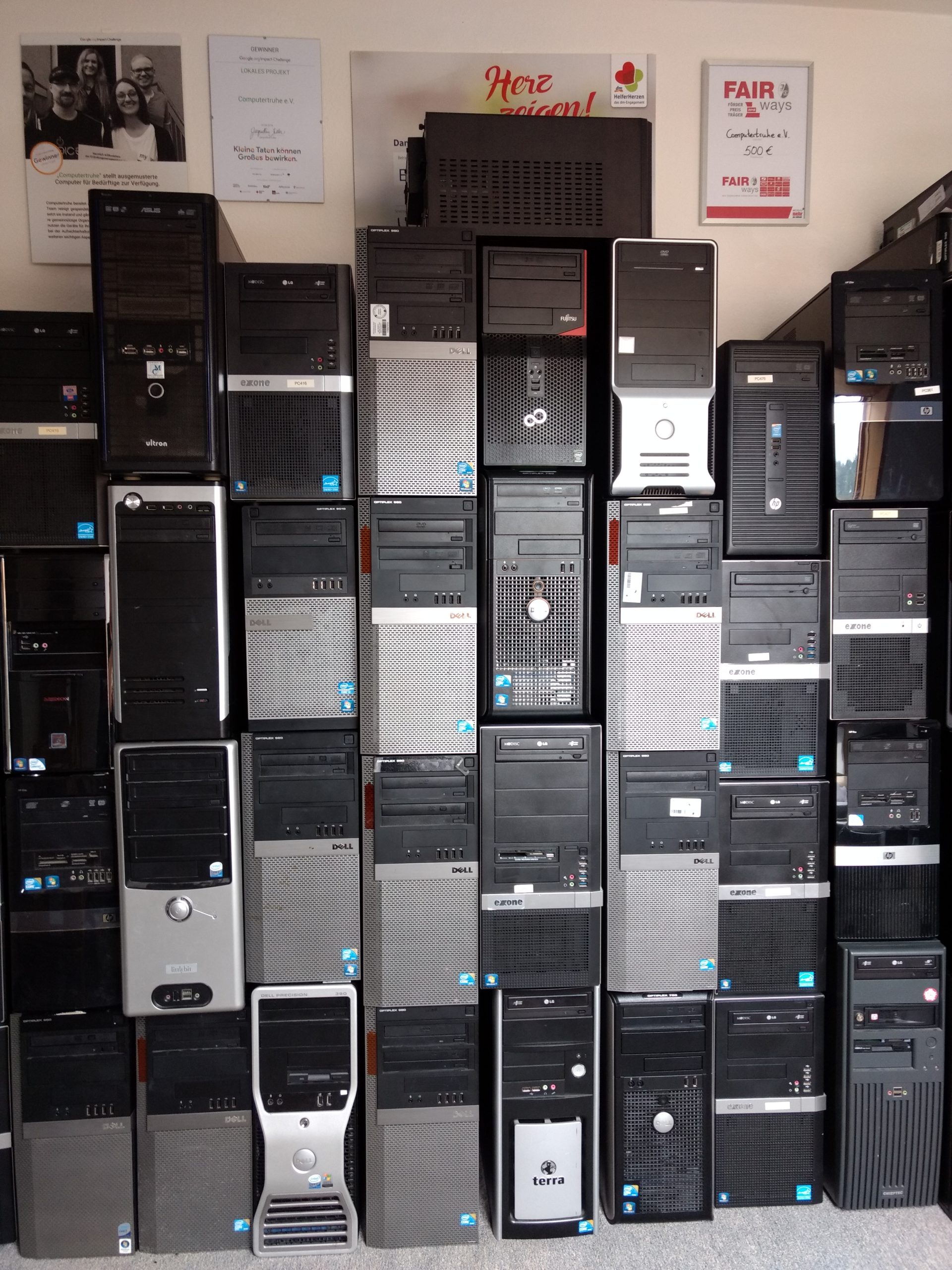 An einer Wand stapeln sich mehr als 30 Desktop-PCs unterschiedlicher Hersteller. Darüber hängen vier Auszeichnungen, die der Verein erhalten hat.