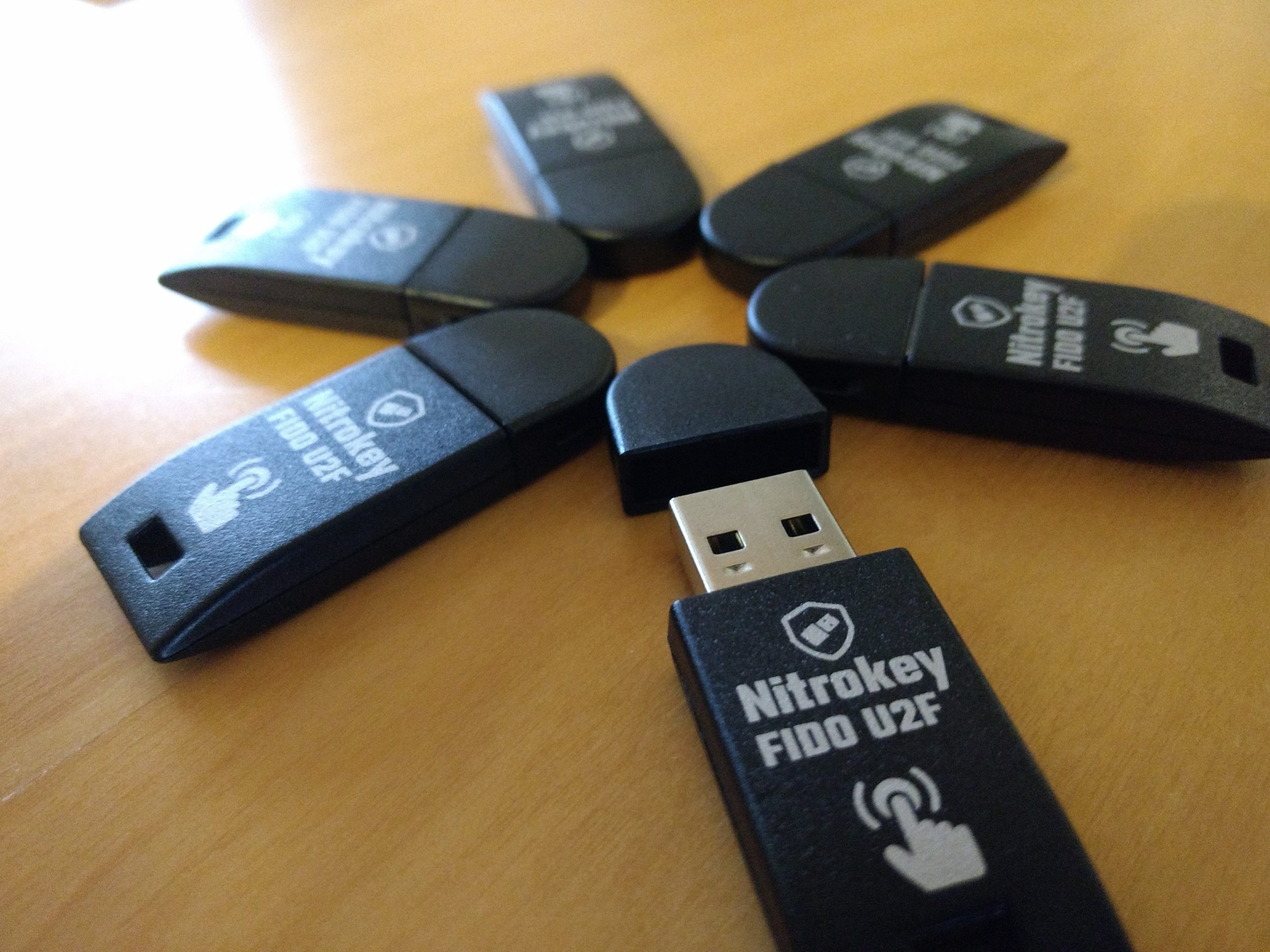 Sechs in einem Ring angeordnete „Nitrokey FIDO U2F“-Sicherheitsschlüssel. Bei einem der USB-Sticks wurde die Schutzkappe des Steckers abgezogen.