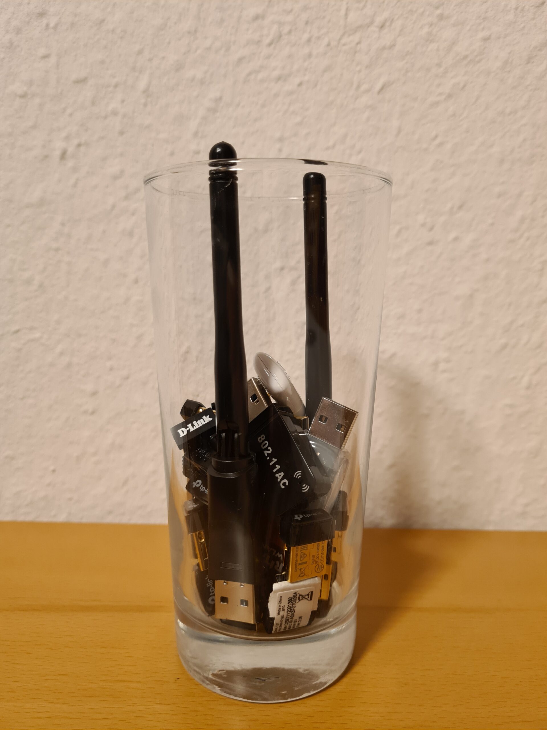 Ein Trinkglas, in dem sich WLAN-USB-Adapter unterschiedlicher Hersteller und Baugrößen befinden.