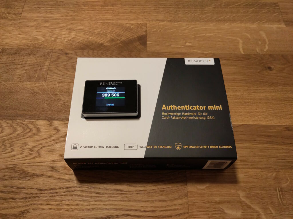 Foto des angeschalteten Gerätes, das auf der Originalverpackung liegt. Es ist nur wenig Zentimeter groß, rechteckig, mit Touch-Display und sieht ein wenig aus wie ein sehr kleines Smartphone.