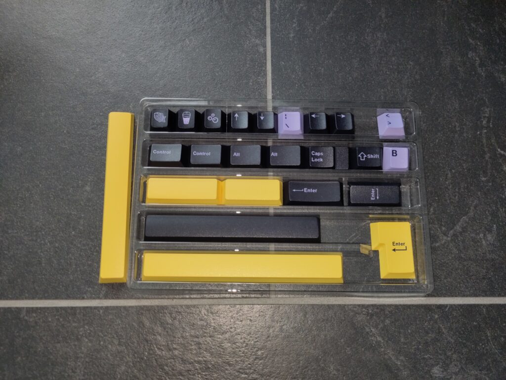 Foto einiger Tastenkappen in unterschiedlichen Farben (flieder, gelb, schwarz). Auf manchen sind diverse Symbole abgebildet.