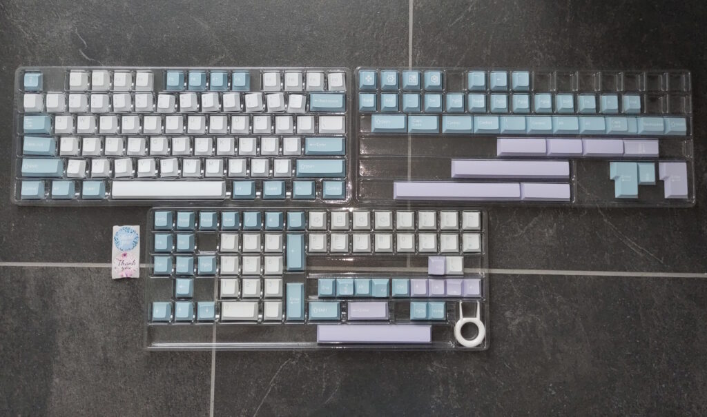 Foto vieler Tastenkappen in unterschiedlichen Pastellfarben (flieder, minze, weiß). Auf manchen sind diverse Symbole abgebildet.