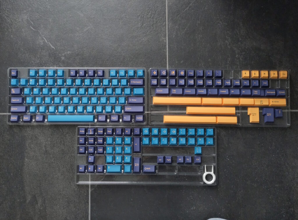 Foto vieler Tastenkappen in unterschiedlichen Farben (lila, grünbläulich, gelb). Auf manchen sind diverse Symbole abgebildet.