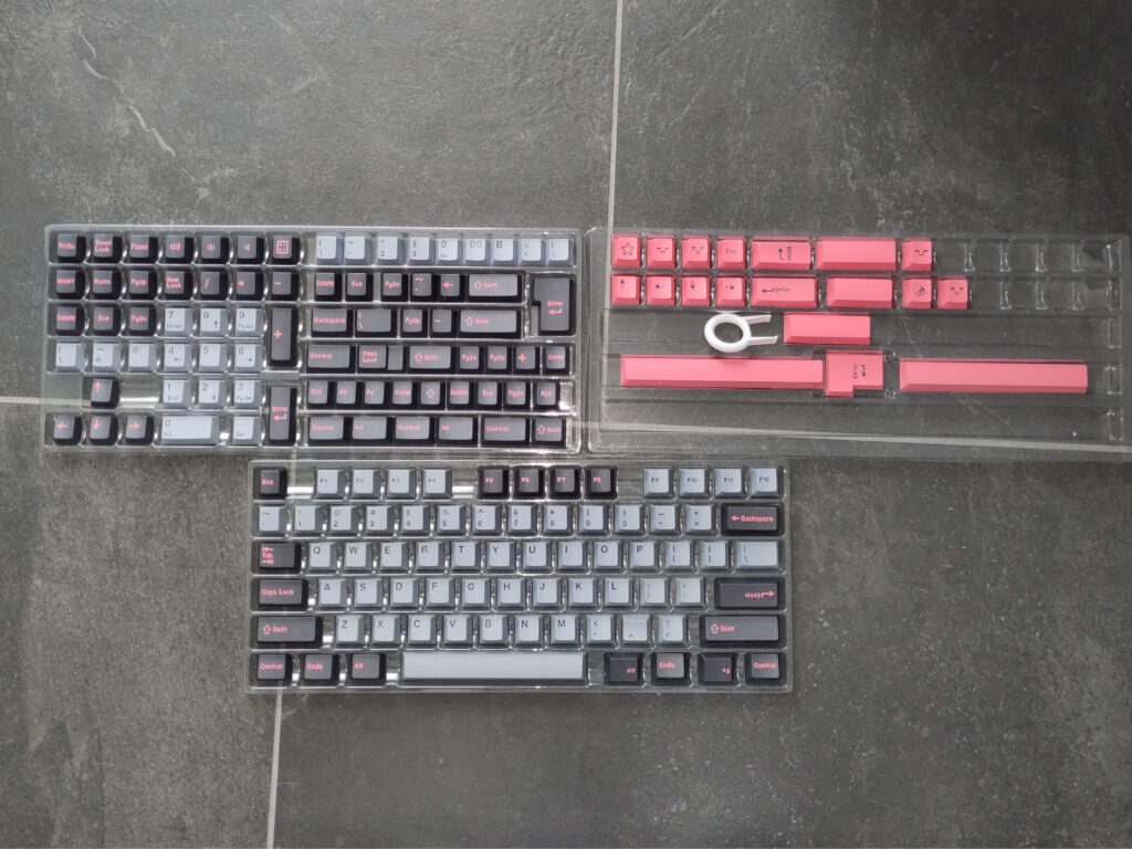 Foto vieler Tastenkappen in unterschiedlichen Farben (hellgrau, dunkelgrau, pink). Auf manchen sind diverse Symbole abgebildet.