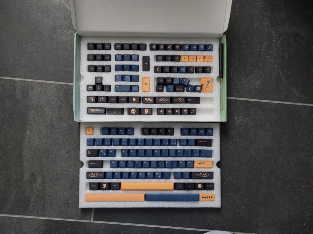 Foto vieler Tastenkappen in unterschiedlichen Farben (schwarz, blau, orange). Auf manchen sind diverse Symbole abgebildet.