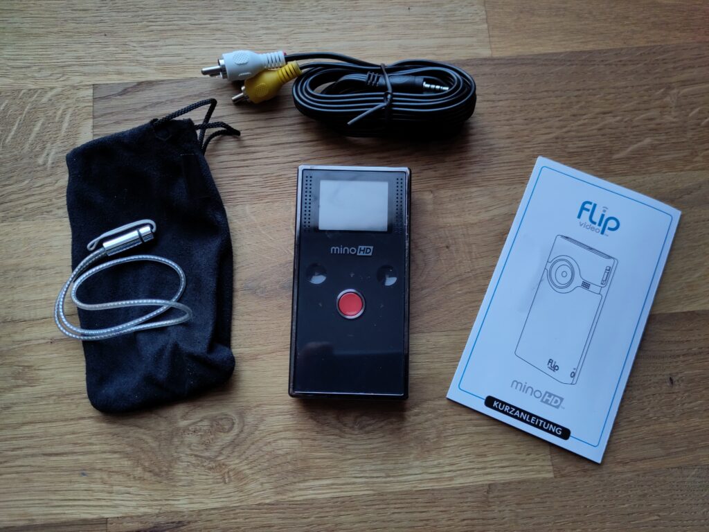 Foto des Camcorders, einer Tasche, einer Handschlaufe, eines Cinch-Videokabels und einer Anleitung.