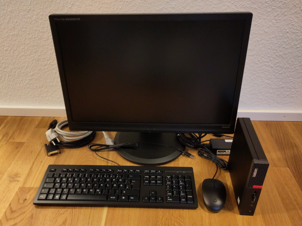 Foto eines kleinen Lenovo ThinkCentre PCs mit Bildschirm, Tastatur, Maus und allen Kabeln. Alles befindet sich in einem hervorragenden Zustand, die Eingabegeräte sind sogar Neuware.