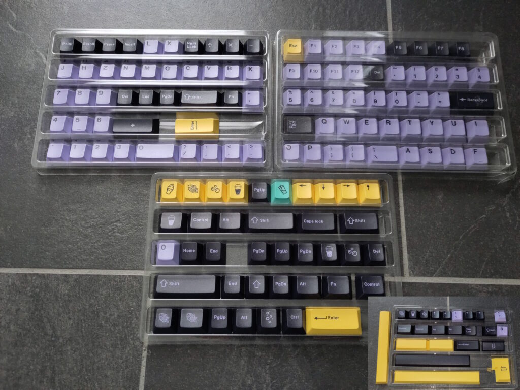 Foto vieler Tastenkappen in unterschiedlichen Farben (lila, gelb, schwarz, türkis). Auf manchen sind Nahrungsmittel abgebildet.