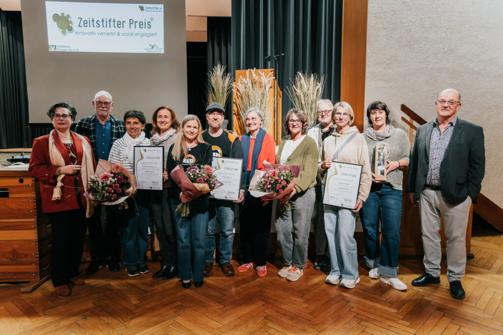 Foto der in der Bildunterschrift genannten Personen. Sie lächeln und die Preisträger*innen halten Blumensträuße und Urkunden in den Händen.