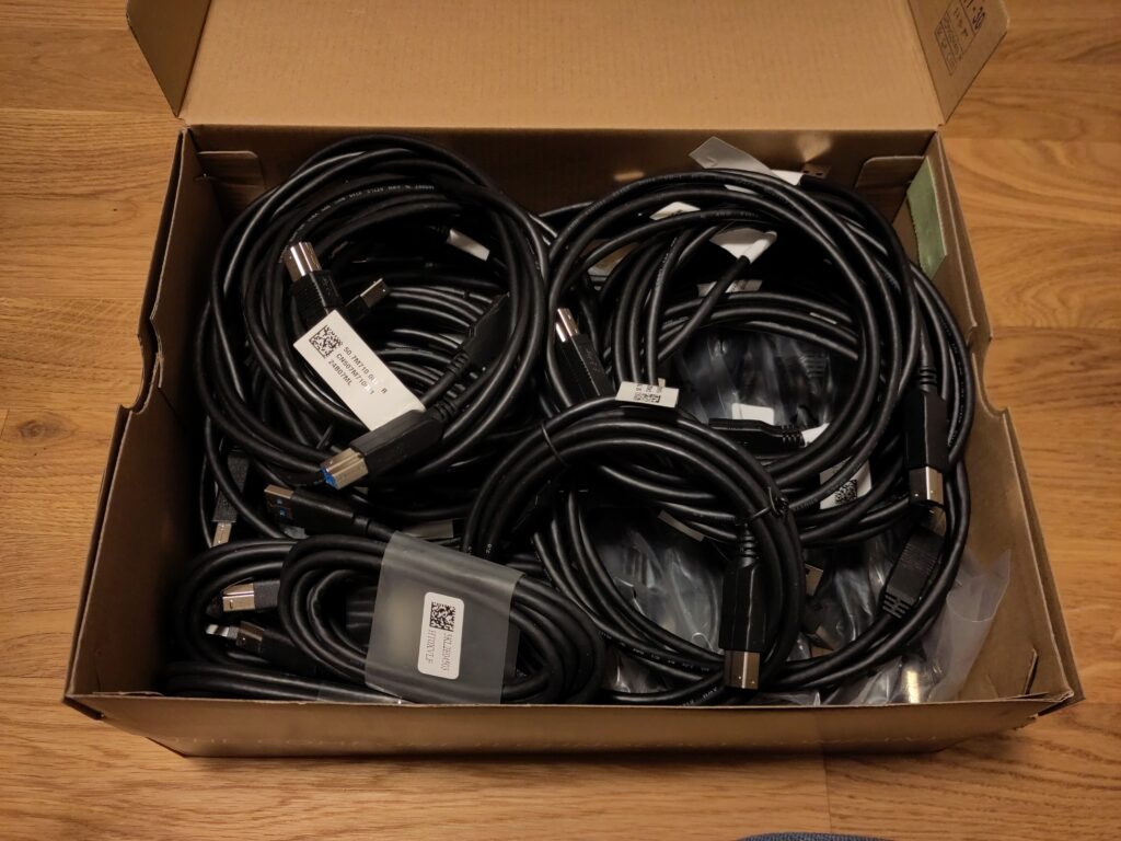 Foto eines Schuhkartons voller USB-Kabel, von denen viele neu sind.