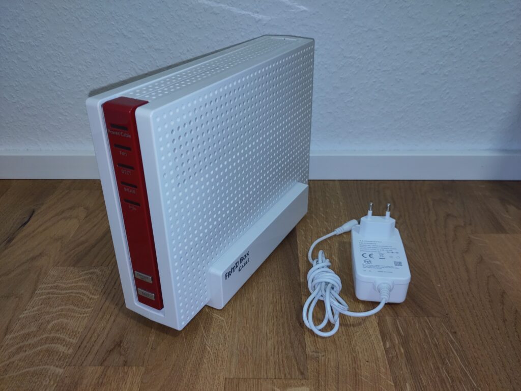 Foto des Routers mit Netzteil. Beides ist in einem hervorragenden Zustand.