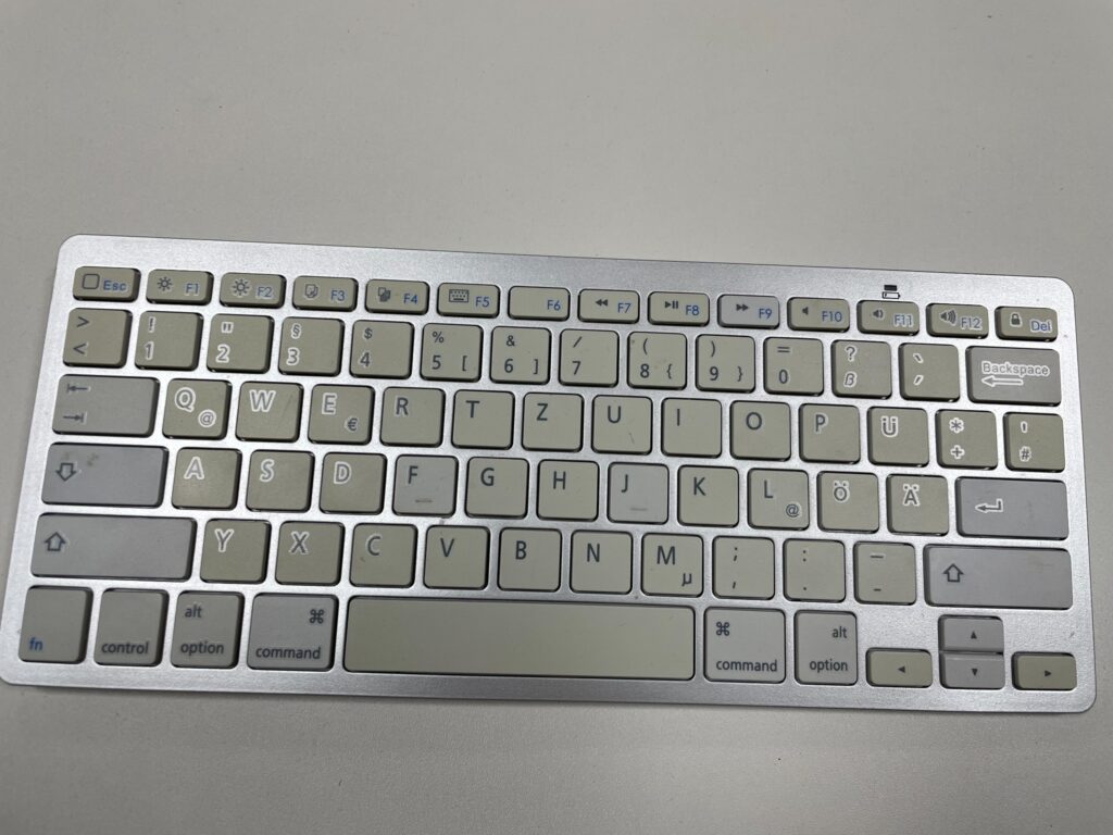 Eine flache silber-weiße Anker Bluetooth-Tastatur mit deutscher QWERTZ-Belegung Apple Layout liegt auf einem hellen Tisch.