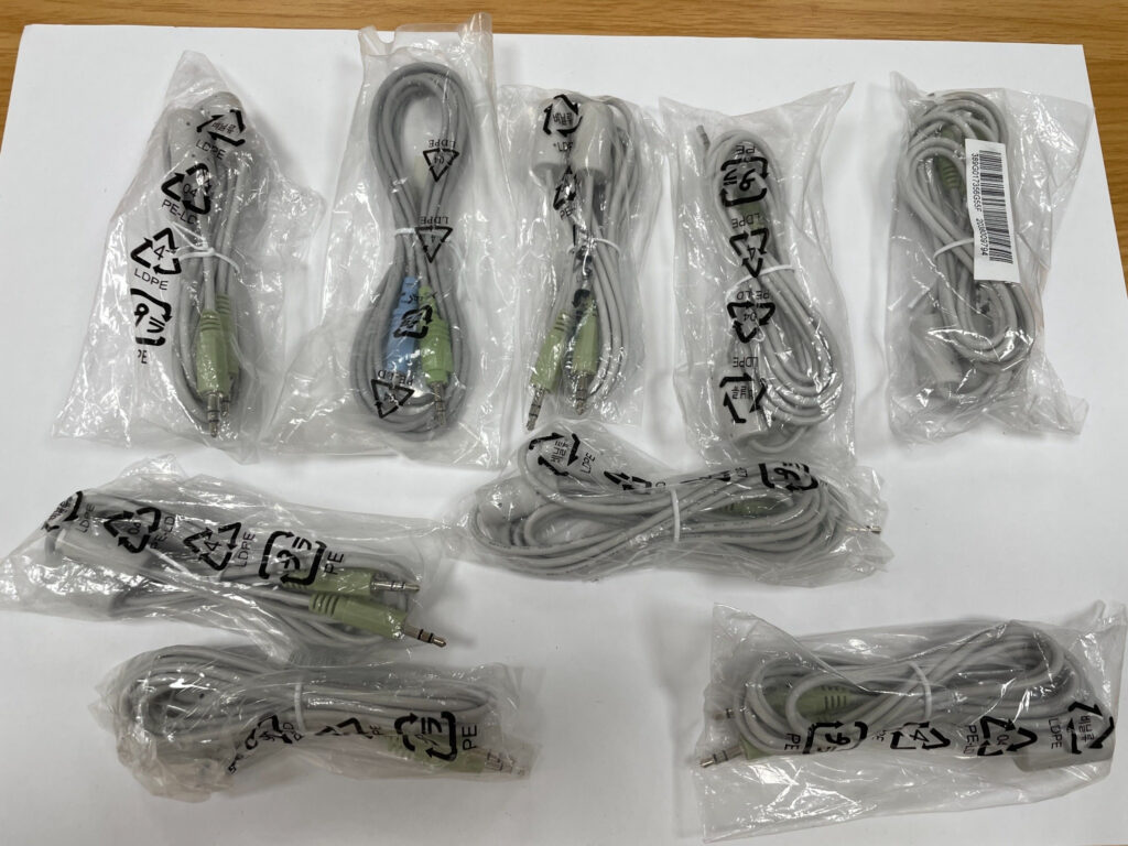 Mehrere graue, einzeln verpackte Audio-Verlängerungskabel mit grünen 3,5-mm-Klinkensteckern und -buchsen.