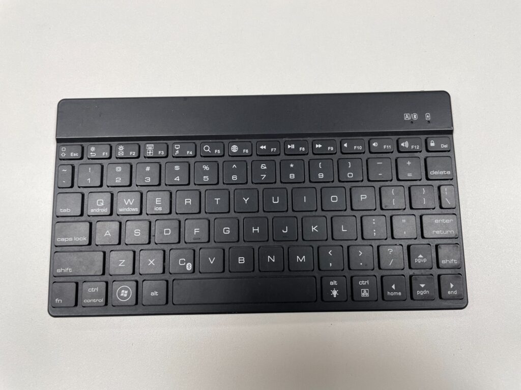 Eine kompakte schwarze Bluetooth-Tastatur mit englischer QWERTY-Belegung liegt auf einem weißen Tisch.
