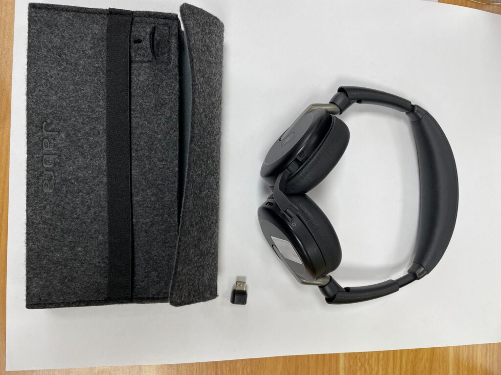 Schwarzes klappbares Jabra-On-Ear-Headset mit kleinem USB-Dongle und grauer Filz-Transporttasche.