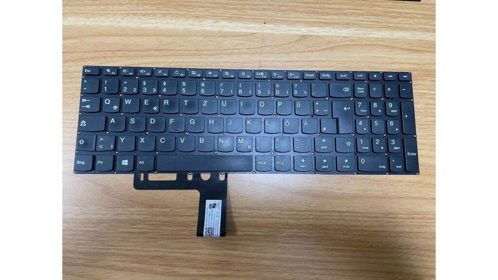 Schwarze kompakte Notebook-Tastatur mit deutschem QWERTZ-Layout, Funktionstasten und angeschlossenem Flachbandkabel.