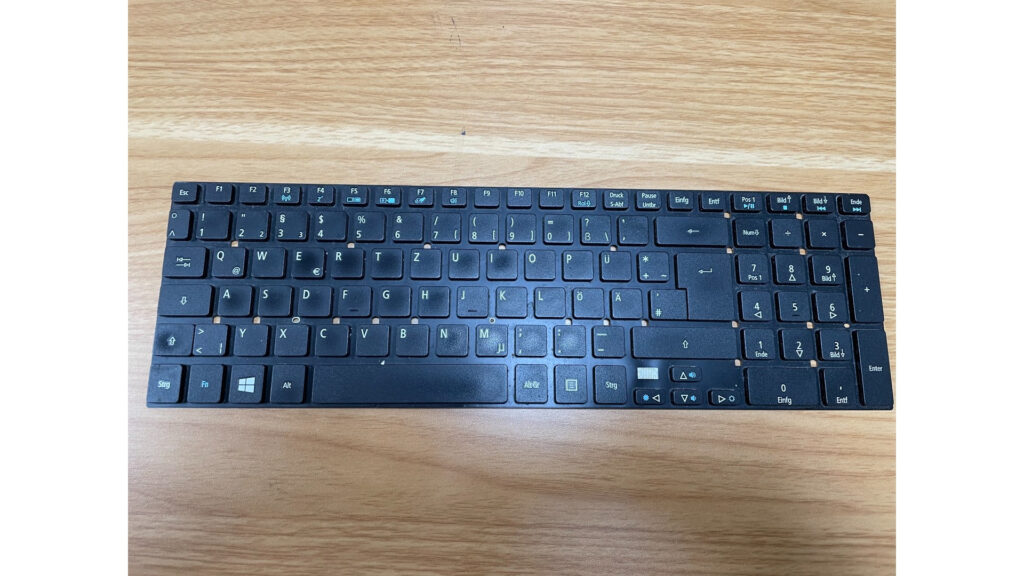 Schwarze kompakte Notebook-Tastatur mit deutschem QWERTZ-Layout, Funktionstasten und angeschlossenem Flachbandkabel.